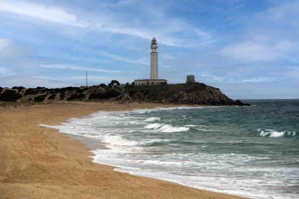 a beach in Andalucia with a lighthouse in the background, 11 Best Andalucia Beach Towns-Costa del Sol Beaches [Playa] Southern Spain, best andalucia beach towns, costa tropical towns, best beaches in southern Spain, best beach towns in Andalucia, best beach towns in Spain, beach towns in Spain, best beach towns Andalucia