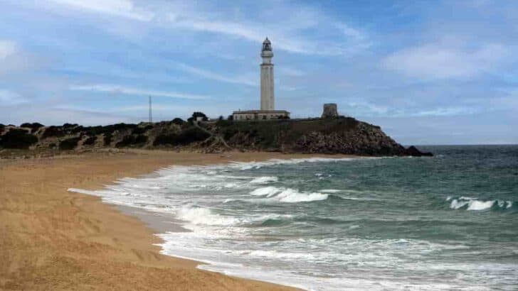 a beach in Andalucia with a lighthouse in the background, 11 Best Andalucia Beach Towns-Costa del Sol Beaches [Playa] Southern Spain