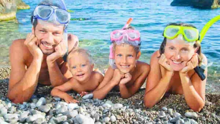 a family in snorkel gear smiling and ready to go snorkeling, Best Snorkeling for Families- Amazing Travel Destinations [Beaches, Beginners, Caribbean]