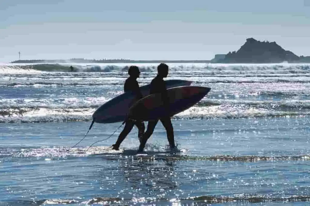 guys walking in water on beach carrying surfboards, 21 [Best] Beach Photo Ideas for Guys- Poses Make The Difference, Mens Beach Poses, beach poses man, beach photo ideas for guys, beach pose ideas, Action Shots on Beach, beach pictures poses man, beach poses for men