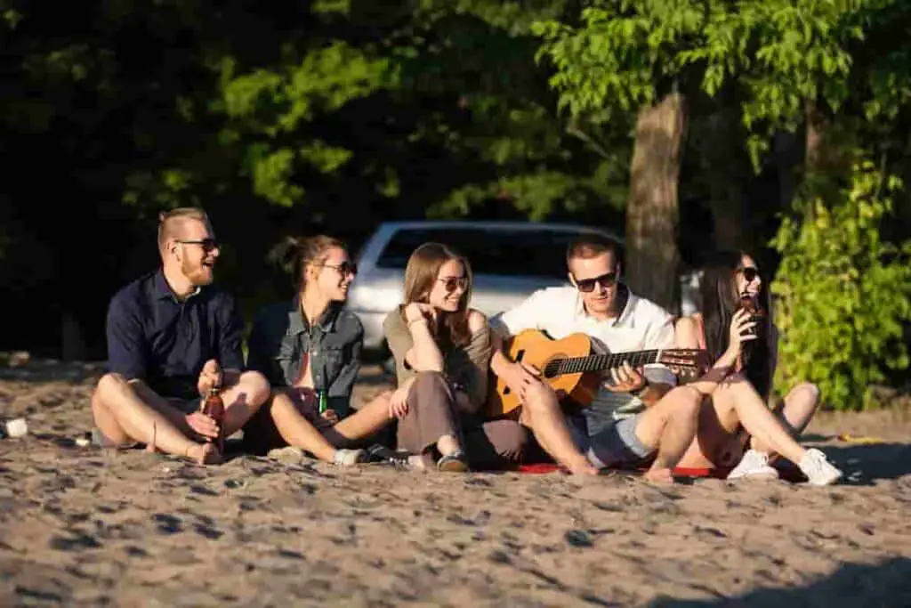 man with friends on beach playing guitar, 21 [Best] Beach Photo Ideas for Guys- Poses Make The Difference, beach photo ideas for guys, beach poses for men, Action Shots on Beach, beach poses man, beach pose ideas, Mens Beach Poses, beach pictures poses man