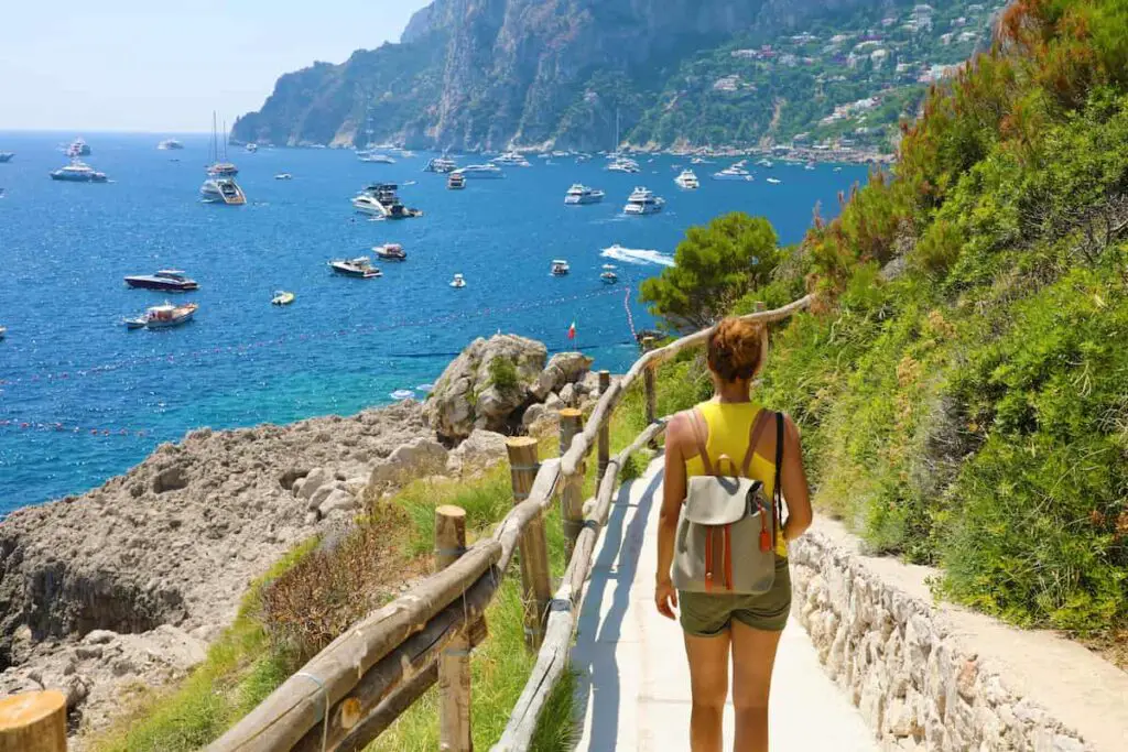 person in yellow shirt with backpack walking along the cliffs and the beach, Italian Coastal Town Charms – Beach Towns Near Naples [Map Plus Best Beach], naples beach italy, best beach towns near naples, beach towns near naples, best towns near naples italy, naples italy beaches, best beach towns near naples italy, towns near naples italy, beach towns near naples italy
