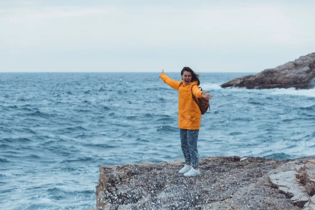 girl standing on a rock on a cloudy day, 9 [Best] Things to Do at the Beach When it’s Cloudy: A Gloomy Day Turned Into Fun, cloudy beach, cloudy beach day, cloudy day at the beach, beach on a cloudy day, overcast beach, activities during cloudy day, what to do on a cloudy day