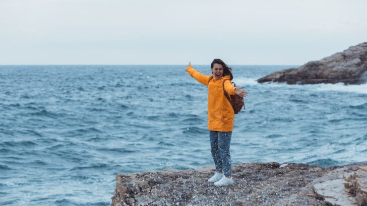 girl standing on a rock on a cloudy day, 9 [Best] Things to Do at the Beach When it&rsquo;s Cloudy: A Gloomy Day Turned Into Fun