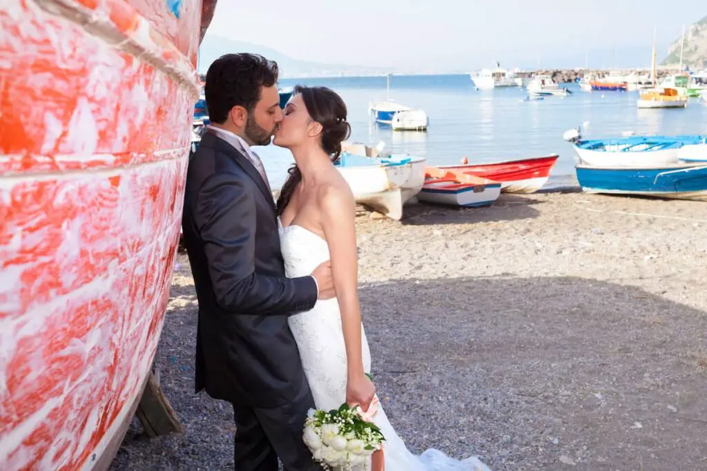 man and woman kissing next to a boat in a boat dock beach area in Italy, Italian Coastal Town Charms – Beach Towns Near Naples [Map Plus Best Beach], beach towns near naples, naples beach italy, naples italy beaches, towns near naples italy, beach towns near naples italy, best beach towns near naples italy, best towns near naples italy, best beach towns near naples