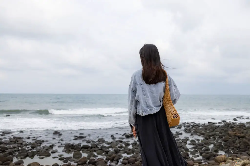 girl looking over the rocky beach on a cloudy day, 9 [Best] Things to Do at the Beach When it’s Cloudy: A Gloomy Day Turned Into Fun, cloudy day at the beach, overcast beach, what to do on a cloudy day, activities during cloudy day, beach on a cloudy day, cloudy beach day, cloudy beach