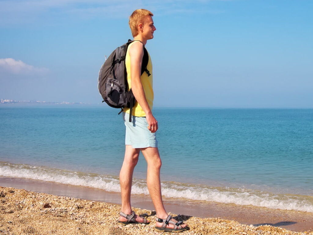 boy with backpack on beach wearing sandals, Experience Comfort: Unveiling the Best Beach Sandals For Men, best beach footwear, best sandals for men, men's sandals, beach thong sandals for men