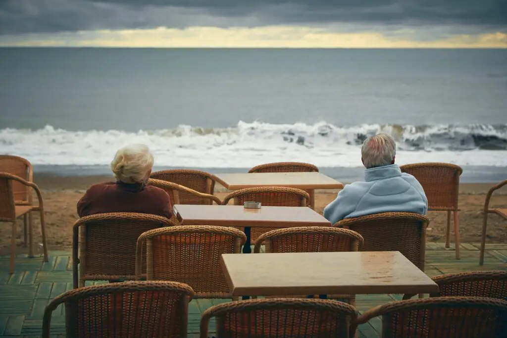 Unrecognizable senior couple admiring foamy ocean from street cafe, 9 [Best] Things to Do at the Beach When it’s Cloudy: A Gloomy Day Turned Into Fun, beach on a cloudy day, cloudy beach day, what to do on a cloudy day, cloudy beach, activities during cloudy day, cloudy day at the beach, overcast beach