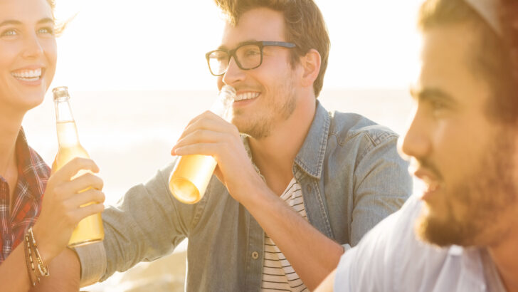 man with friends sitting on beach with bottle in hand, 21 [Best] Beach Photo Ideas for Guys- Poses Make The Difference