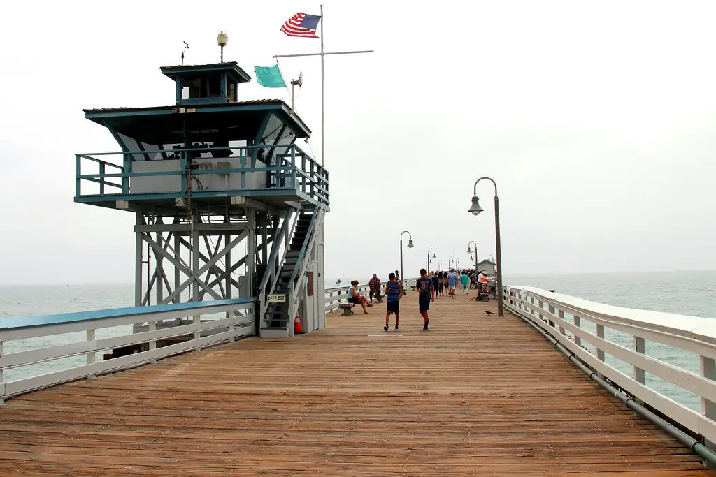 people walking on the pier boardwalk on a cloudy day, 9 [Best] Things to Do at the Beach When it’s Cloudy: A Gloomy Day Turned Into Fun, what to do on a cloudy day, beach on a cloudy day, activities during cloudy day, cloudy beach, overcast beach, cloudy day at the beach, cloudy beach day