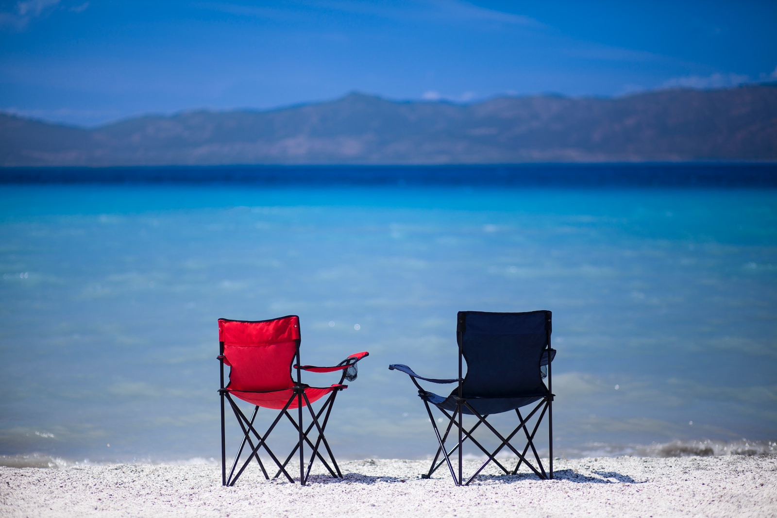 red and black folding chair on white sand during daytime, 11 Beach Travel Essentials to Pack – Minimalist Approach [Plus Packing List], essential beach items, Beach Footwear Choices, minimalist packing for beach vacation, beach trip essentials, Water-Resistant Tech Gear, UV-Protection Essentials, Minimalist Beach Packing