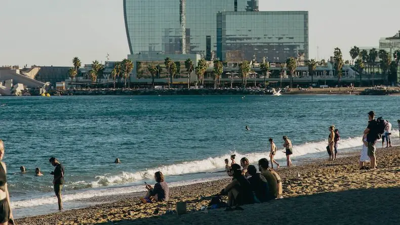 a group of people sitting on top of a sandy beach at La Barceloneta Spain, 2024 Best Towns Near Barcelona With A Beach: 15 Tops Spots, best beach towns near barcelona, cities near barcelona, best coastal towns near barcelona, barcelona beach, barcelona beach resorts, beach towns near barcelona, beach resorts near barcelona