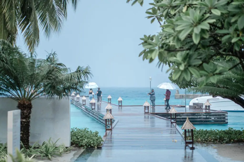 People Walking Wooden Jetty while Raining, Making the Most of a Rainy Day at the Beach: Fun Rainy Day Activities to Enjoy Despite the Weather, rainy beach day, beach in the rain, rainy day beach activities, what to do at the beach when it rains, rainy beach, rainy day at the beach, rainy day beach activities
