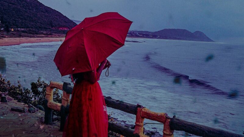 Photo of Person Wearing Red Dress While Holding Red Umbrella, Making the Most of a Rainy Day at the Beach: Fun Rainy Day Activities to Enjoy Despite the Weather, rainy beach day, beach in the rain, rainy day beach activities, what to do at the beach when it rains, rainy beach, rainy day at the beach, rainy day beach activities
