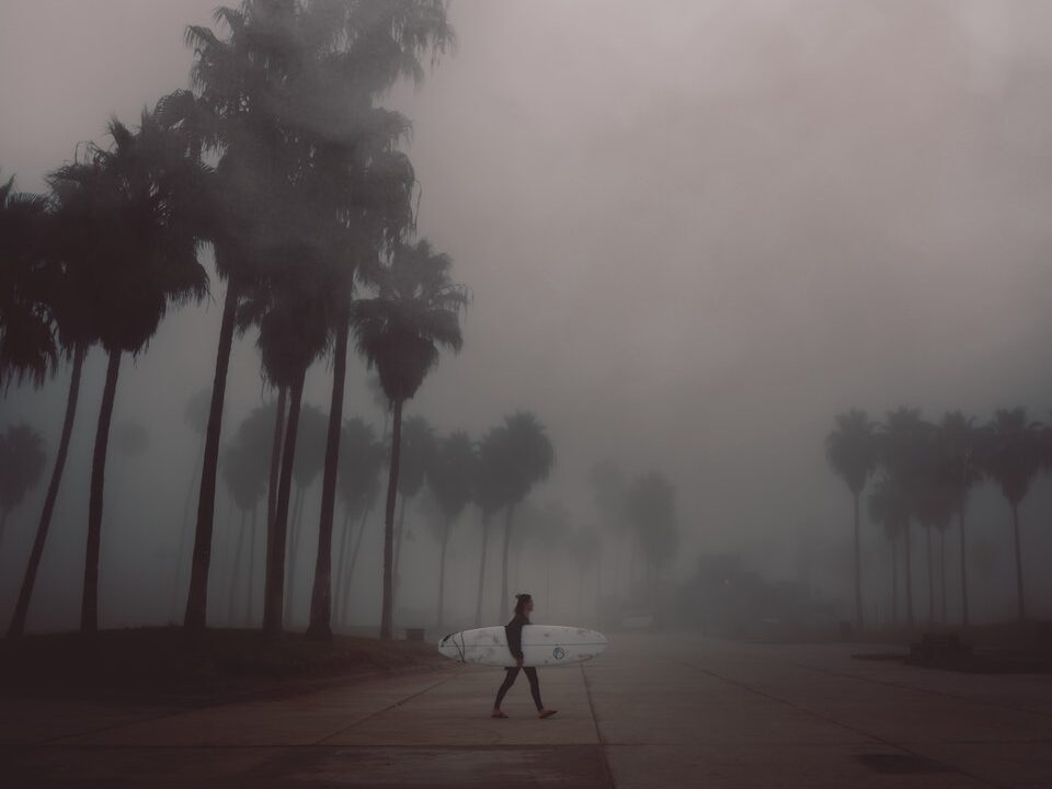 Surfer Walking on Road in cloudy and rainy conditions with his surfboard, Making the Most of a Rainy Day at the Beach: Fun Rainy Day Activities to Enjoy Despite the Weather, rainy day at the beach, what to do at the beach when it rains, rainy beach day, rainy day beach activities, beach in the rain, rainy beach, rainy day beach activities
