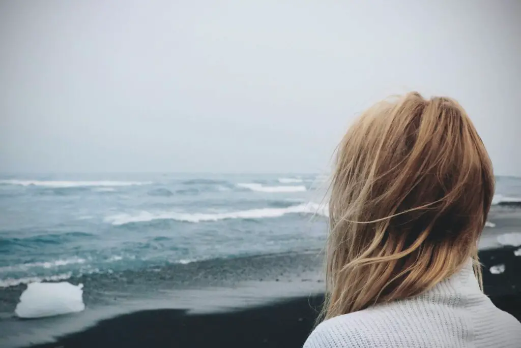 Woman Standing on Shoreline on a cloudy day, Making the Most of a Rainy Day at the Beach: Fun Rainy Day Activities to Enjoy Despite the Weather, rainy day beach activities, rainy beach, rainy beach day, rainy day at the beach, rainy day beach activities, what to do at the beach when it rains, beach in the rain