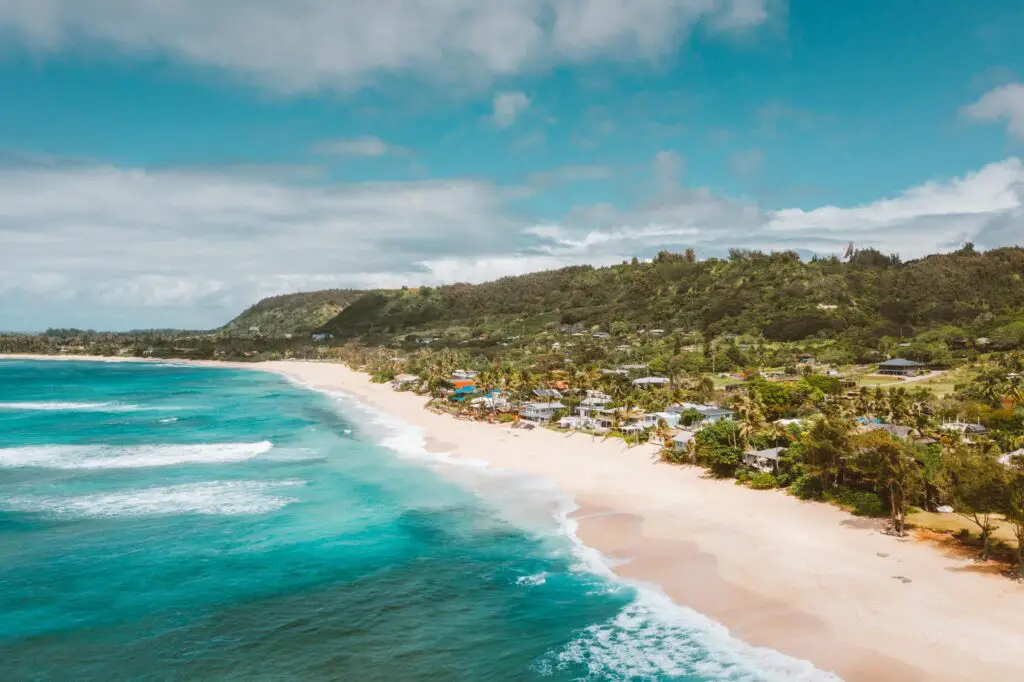 an aerial shot of an aqua blue beach on the left and beach houses on the right, How Much Does it Cost to Rent a Beach House? Renting vs. Buying: [Surprising Facts] Guide to Vacation Rentals, how much does it cost to rent a beach house for a week, how much does a beach house cost, how much is it to rent a beach house, how much does a beach house cost to rent, how much are beach houses to rent, how much to rent a beach house, how much is a beach house