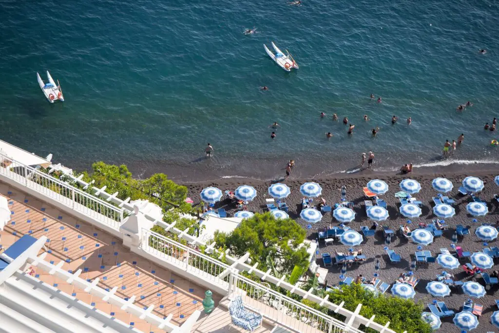 aerial view of people on beach during daytime with colorful blue and white beach umbrellas, Italian Coastal Town Charms – Beach Towns Near Naples [Map Plus Best Beach], naples beach italy, best beach towns near naples, beach towns near naples, best towns near naples italy, naples italy beaches, best beach towns near naples italy, towns near naples italy, beach towns near naples italy
